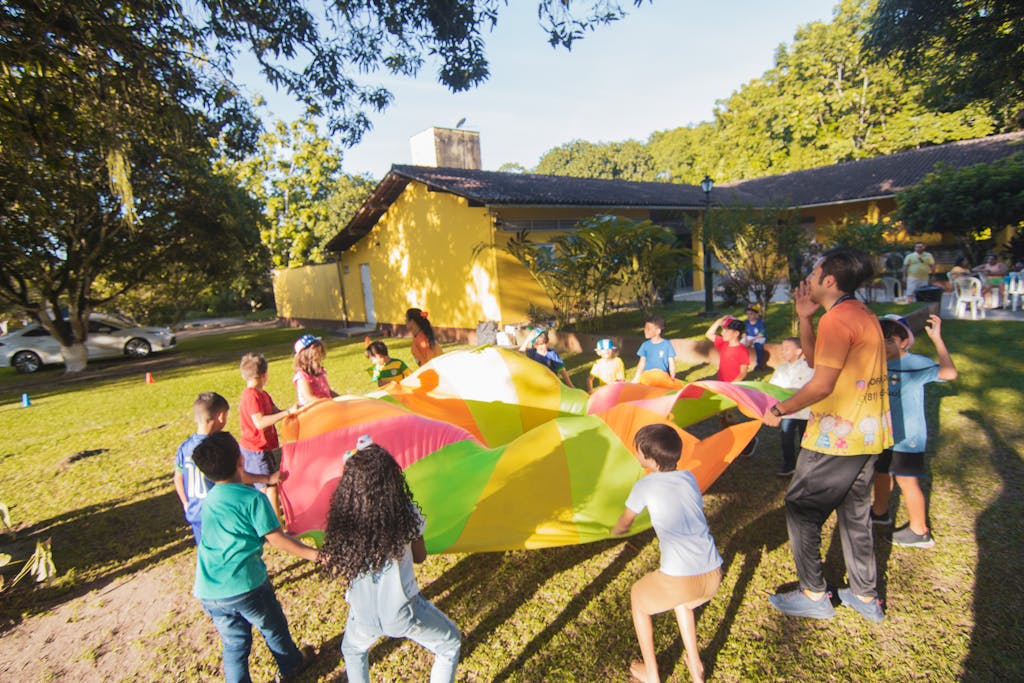 Group of children playing with a colorful parachute outside during a sunny day party.